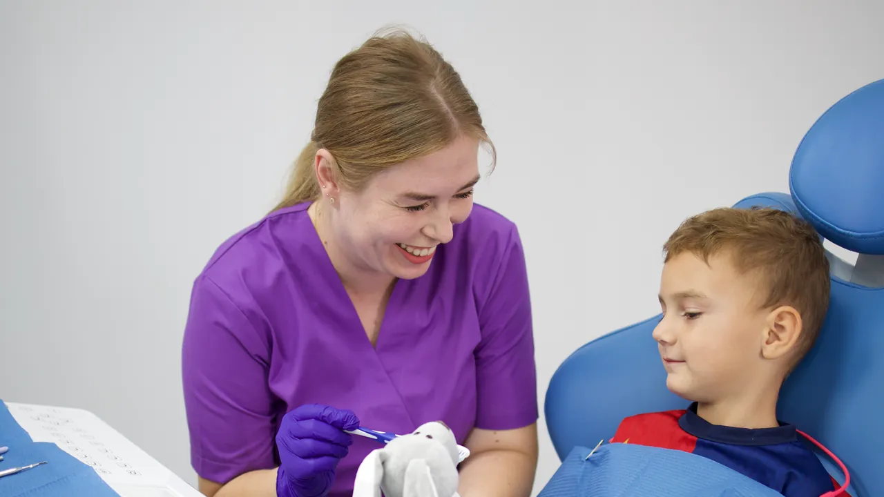 Medic stomatolog arătându-i unui copil cum se periază dinții, pe o jucărie de pluș