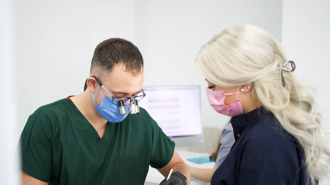Medic stomatolog cu lupe de mărire tratând un pacient, cu o colegă alături
